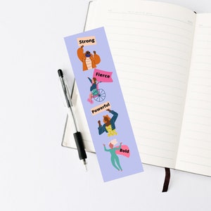 May include: A purple bookmark with illustrations of women holding signs with the words "Strong", "Fierce", "Powerful", and "Bold".