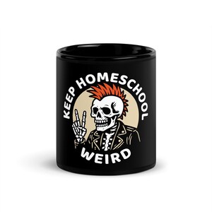 May include: Black ceramic mug featuring a skeleton with a mohawk and leather jacket, giving a peace sign. The text "KEEP HOMESCHOOL WEIRD" is printed around the skeleton in a circular design. The background is a tan circle.