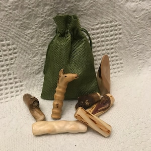 May include: A set of wooden figurines, including a giraffe, in a green burlap bag. The figurines are made of natural wood and have a rustic, handcrafted look.