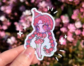 May include: A holographic sticker featuring a cartoon character with red hair, a pink dress, and a heart-shaped hat. The character has large eyes and is holding a heart in their hand. The sticker is surrounded by a white border and has a glittery finish.