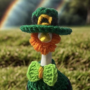 May include: A handcrafted St. Patrick's Day decoration. It features a crochet leprechaun figure with a green hat, orange beard, and green bow tie, perched atop a black pot filled with coins. The pot is sitting on a grassy surface.