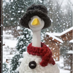 Peut inclure: Une figurine d'oie bonhomme de neige fantaisiste avec un chapeau noir, une écharpe rouge et des boutons. L'oie a un corps blanc, un bec jaune et une base verte et jaune. Le fond montre une scène hivernale enneigée.