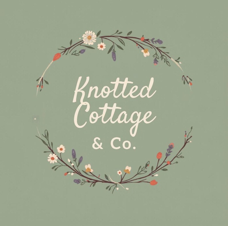 Pu&ograve; includere: Un grafico quadrato verde salvia che presenta il testo bianco Knotted Cottage & Co. centrato all'interno di una ghirlanda circolare di elementi botanici disegnati a mano, inclusi piccoli fiori bianchi, boccioli viola e accenti arancioni.
