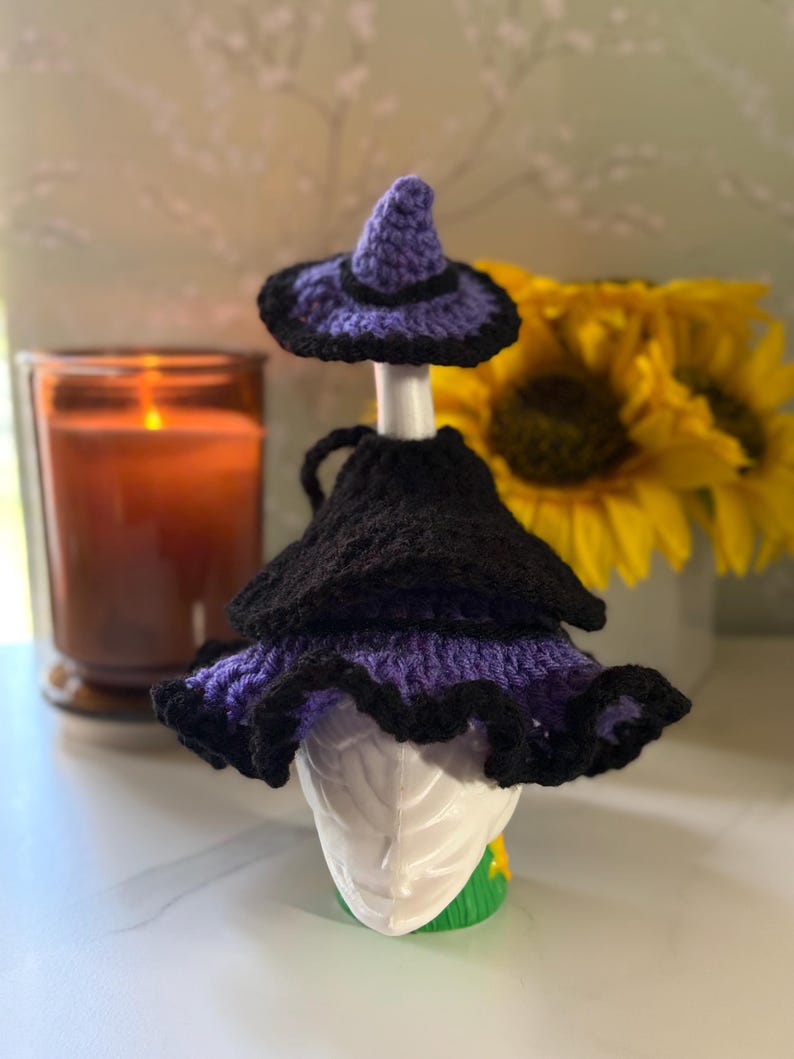 Pu&ograve; includere: Un copribottiglia a forma di cappello da strega all'uncinetto viola e nero, con corona a punta e tesa larga arricciata. Il cappello &egrave; progettato per adattarsi al collo di una bottiglia, con un cappellino abbinato posizionato sul tappo.