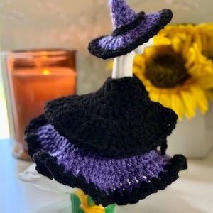 Pu&ograve; includere: Un completo all'uncinetto per una statuetta di oca composto da un cappello da strega nero e viola e un vestito a strati. Il vestito presenta un corpetto nero con una gonna viola e nera a balze. Il completo &egrave; progettato per un'oca bianca.