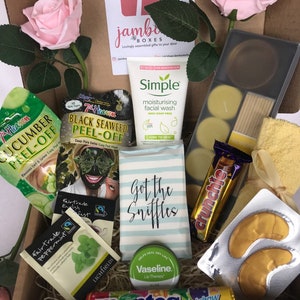 May include: A gift box filled with various self-care items, including face masks, tea bags, lip balm, eye masks, and candy. The box also includes a small card that says "Got the Sniffles".