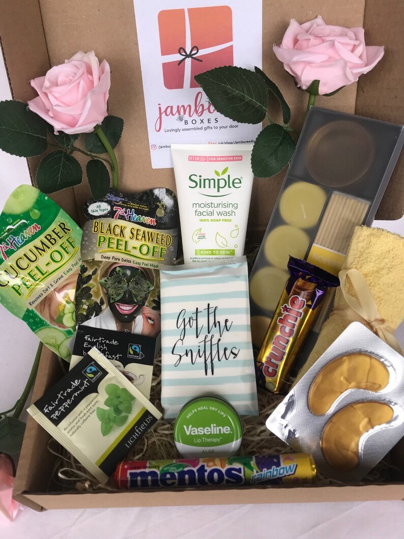 May include: A gift box filled with various self-care items, including face masks, tea bags, lip balm, eye masks, and candy. The box also includes a small card that says "Got the Sniffles".