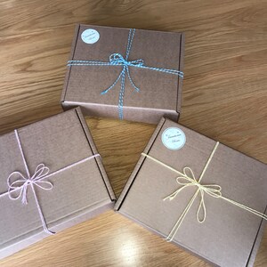 May include: Three brown cardboard boxes tied with string and bows. The boxes are tied with different colored string: blue, pink, and yellow. Each box has a round label with the text "Treasure Box" on it.
