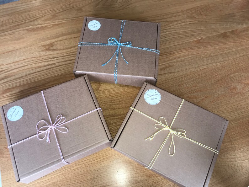May include: Three brown cardboard boxes tied with string and bows. The boxes are tied with different colored string: blue, pink, and yellow. Each box has a round label with the text "Treasure Box" on it.