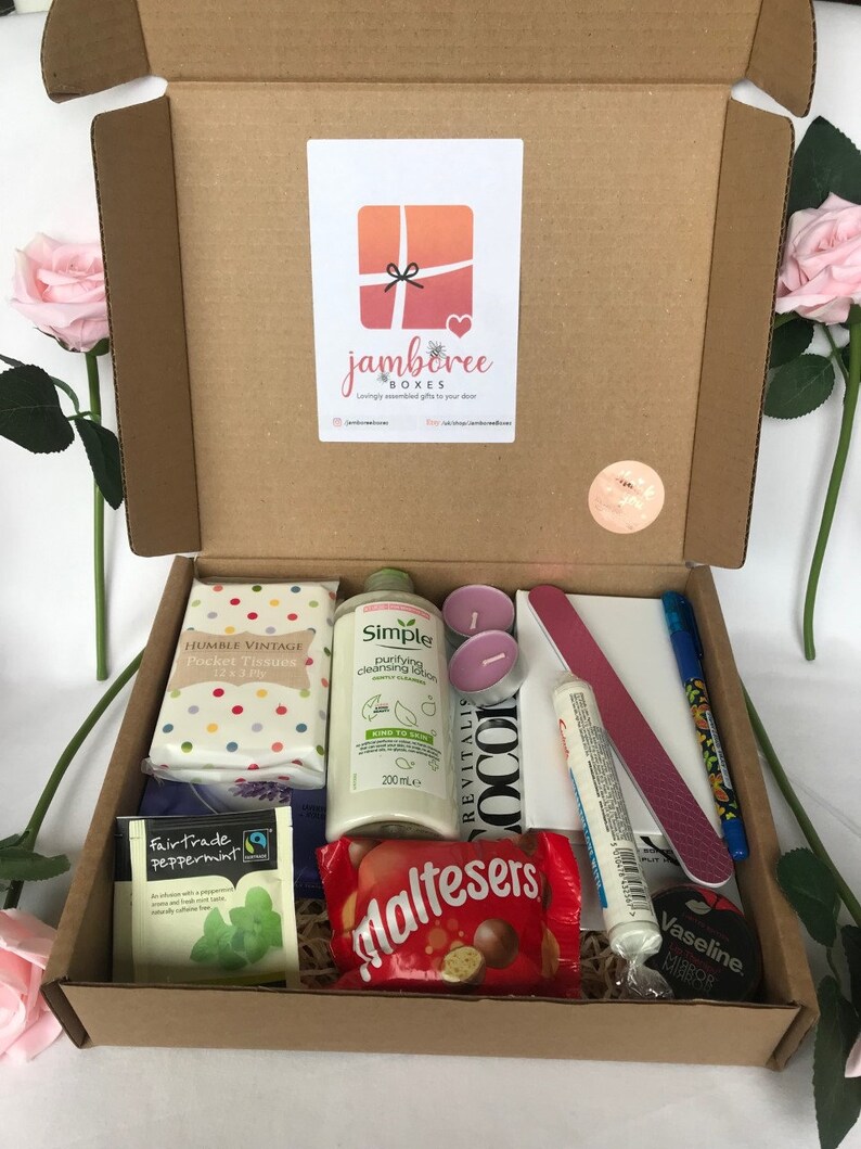 May include: A brown cardboard box filled with a variety of gifts, including a bottle of Simple Purifying Cleansing Lotion, a pack of Humble Vintage Pocket Tissues, a box of Maltesers chocolates, a pack of Fairtrade Peppermint tea, two pink candles, a nail file, a tube of Vaseline lip balm, and a blue pen.