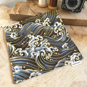 May include: Square fabric item with a repeating wave pattern in shades of brown, blue, and gold. The design features stylized waves and foam. The item has a white tag that reads "mind be kind".