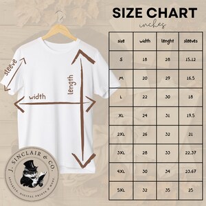 Pode incluir: Tabela de tamanhos para uma camiseta branca com um gr&aacute;fico marrom de um gato usando um chap&eacute;u de coco e lendo um livro. A tabela mostra o tamanho, a largura, o comprimento e o comprimento da manga em polegadas.