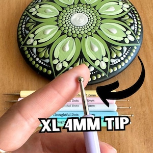 May include: A close-up of a hand holding a purple dotting tool with a 4mm tip. The tool is labeled "XL 4MM TIP". The hand is holding the tool over a set of dotting tools with different sized tips. The tools are labeled with their sizes in millimeters. The background is a green and white mandala design.