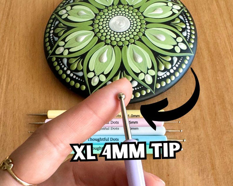 May include: A close-up of a hand holding a purple dotting tool with a 4mm tip. The tool is labeled "XL 4MM TIP". The hand is holding the tool over a set of dotting tools with different sized tips. The tools are labeled with their sizes in millimeters. The background is a green and white mandala design.