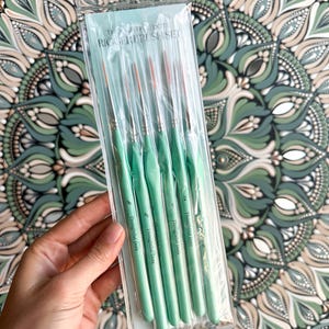 Op de afbeelding: Een set van zes groene verfkwasten met de tekst "Thoughtful Dots" en "Rigger Brush Set" op de verpakking. De kwasten zijn verpakt in een doorzichtige plastic hoes.