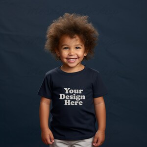K&ouml;nnte beinhalten: Ein kleines Kind tr&auml;gt ein marineblaues T-Shirt mit dem Text "Your Design Here" in Wei&szlig;. Das Kind hat lockiges braunes Haar und l&auml;chelt.