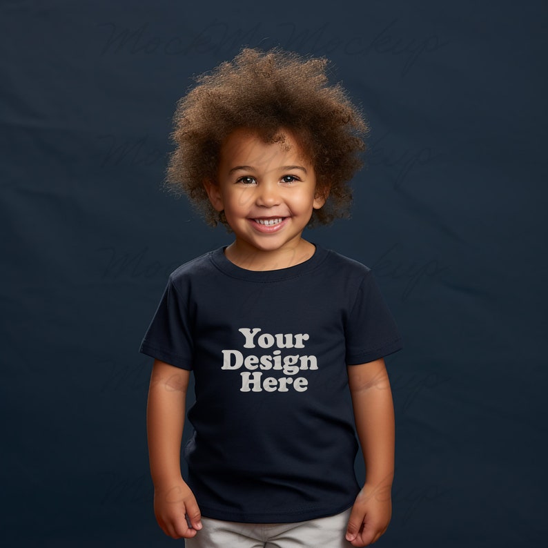 K&ouml;nnte beinhalten: Ein kleines Kind tr&auml;gt ein marineblaues T-Shirt mit dem Text "Your Design Here" in Wei&szlig;. Das Kind hat lockiges braunes Haar und l&auml;chelt.