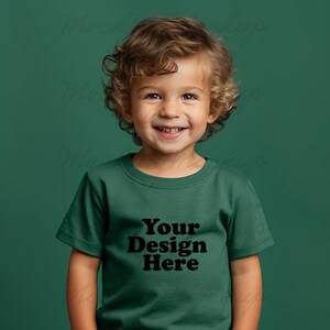 K&ouml;nnte beinhalten: Ein kleines Kind tr&auml;gt ein gr&uuml;nes T-Shirt mit dem Aufdruck "Your Design Here" auf der Vorderseite. Das Kind l&auml;chelt und schaut in die Kamera.
