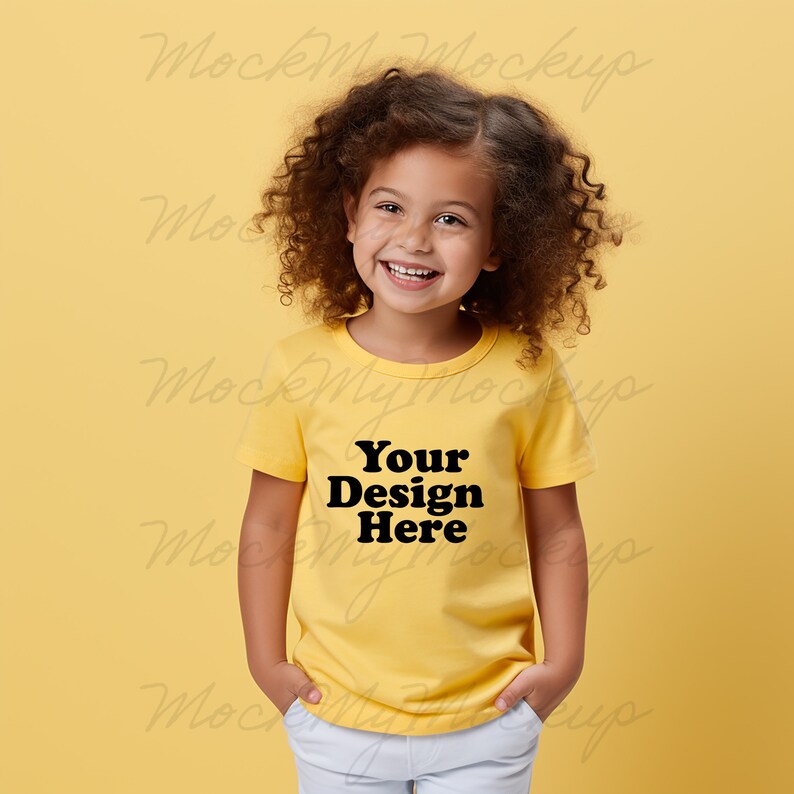 K&ouml;nnte beinhalten: Ein junges Kind tr&auml;gt ein gelbes T-Shirt mit dem Text "Your Design Here" in Schwarz. Das Kind l&auml;chelt und hat lockiges braunes Haar.