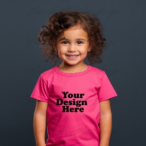 K&ouml;nnte beinhalten: Ein kleines Kind tr&auml;gt ein pinkfarbenes T-Shirt mit dem Aufdruck "Your Design Here" in Schwarz.