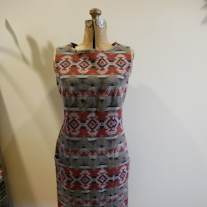 May include: A sleeveless dress with a geometric pattern in shades of red, blue, and gray. The dress has a fitted silhouette and two pockets.