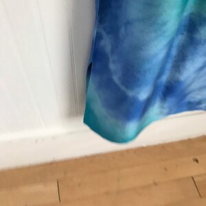Puede incluir: Una tela azul y verde de te&ntilde;ido anudado con fondo blanco. La tela est&aacute; doblada y el borde inferior es visible.