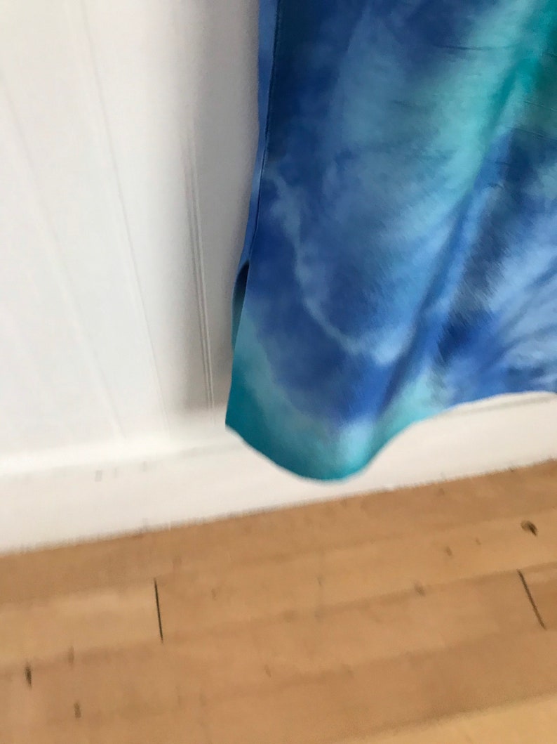 Puede incluir: Una tela azul y verde de te&ntilde;ido anudado con fondo blanco. La tela est&aacute; doblada y el borde inferior es visible.
