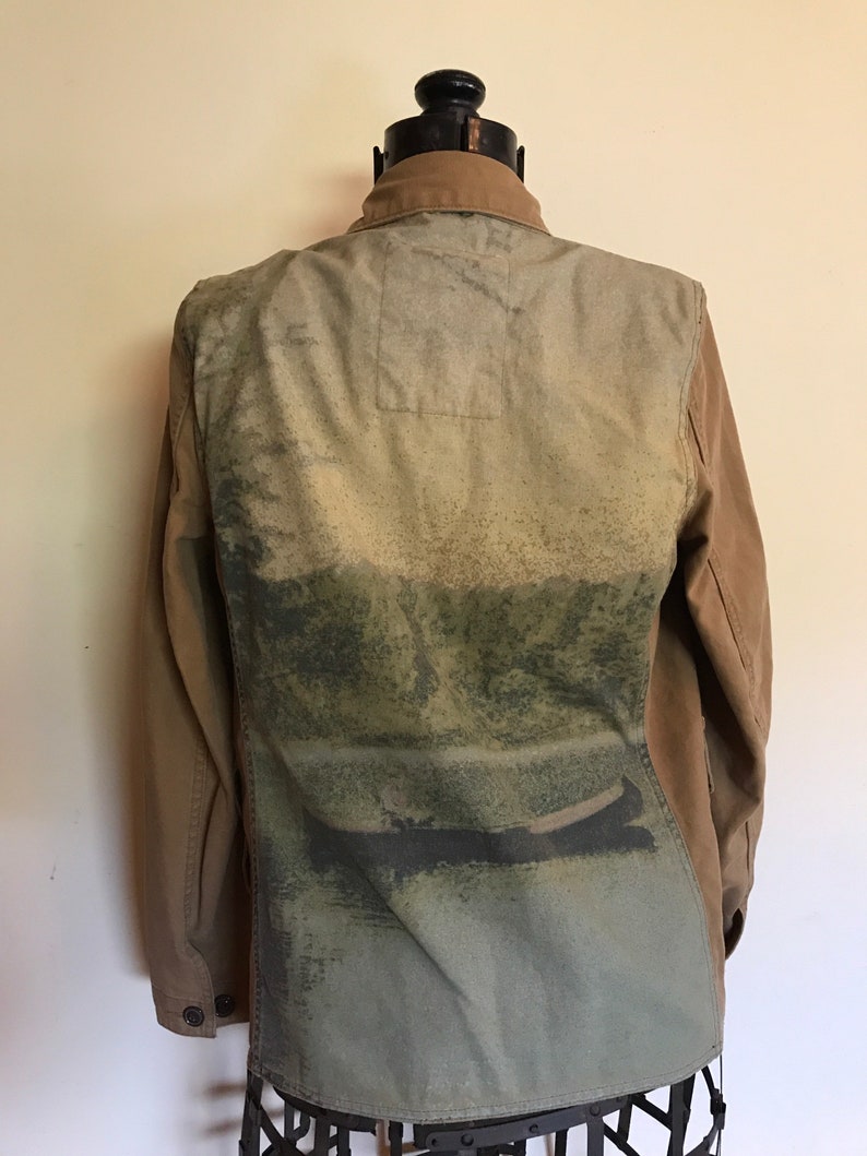 May include: A brown and green utility jacket with a faded image of a landscape on the back. The jacket has a button-up front and long sleeves.