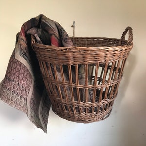 May include: A brown wicker basket with a woven pattern hangs on a wall. A brown and beige patterned blanket is draped over the side of the basket.