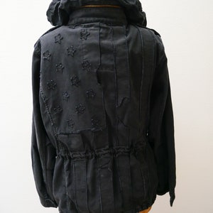 May include: Black hooded jacket with a distressed American flag design on the back. The jacket has a drawstring waist and long sleeves.