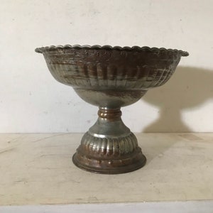 May include: A silver and copper bowl with an ornate design sits on a pedestal. The bowl has a scalloped edge and the pedestal has a fluted design.