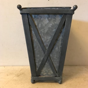 May include: A black metal planter with a galvanized metal insert. The planter has a rectangular shape with a cross-hatch design on the front.