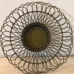 May include: A round, antique-style metal basket with a woven design. The basket has a circular shape with a flat, solid base and a decorative, openwork rim. The metal has a tarnished, aged appearance.