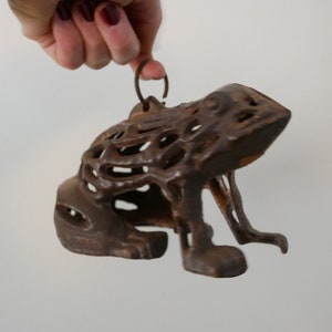 May include: A cast iron frog figurine with a decorative, openwork design. The frog has a loop on its back for hanging.