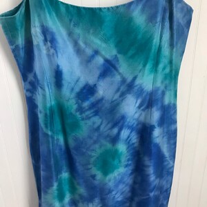 Puede incluir: Un vestido maxi de color azul y verde con estampado tie-dye y tirantes finos. El vestido est&aacute; hecho de una tela sedosa y tiene una silueta fluida.