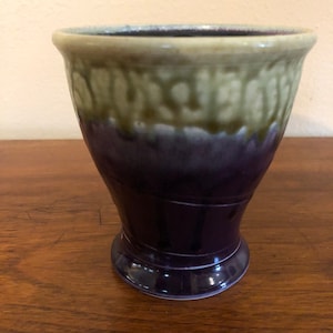 Può includere: Un vaso in ceramica con una smaltatura verde e viola. Il vaso ha un'ampia apertura e una base stretta.