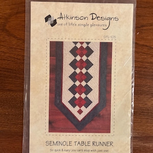 May include: A package showing an Atkinson Designs pattern for a Seminole table runner. The design features a geometric pattern with red, black, and white diamonds. The text reads, "So quick & easy you can't stop with just one!"