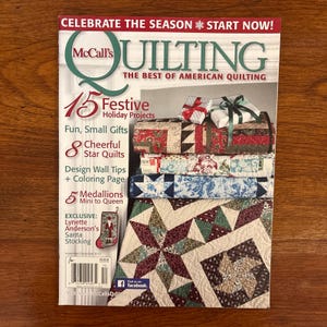 Könnte beinhalten: Das Cover des McCall's Quilting Magazins mit einer Auswahl an bunten Quilts und Geschenkverpackungen. Die Überschrift lautet „Celebrate the Season“ und bewirbt festliche Ferienprojekte, Sternquilts und Designtipps für Quilter.