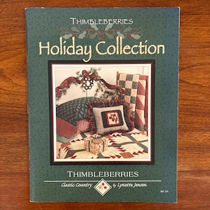 Könnte beinhalten: Buchcover für die "Thimbleberries Holiday Collection" mit einer gemütlichen Innenszene mit Quilts und Kissen. Das Cover ist dunkelgrün mit weißem und rotem Titel, der Name des Autors ist sichtbar.