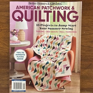 Könnte beinhalten: Das Cover des Magazins "Better Homes & Gardens American Patchwork & Quilting". Das Cover zeigt einen bunten Quilt, der über einem orangefarbenen Sessel drapiert ist. Der Quilt hat ein geometrisches Muster aus Dreiecken in verschiedenen Farben. Der Text enthält "15 Projects to Jump-Start Your Summer Sewing."