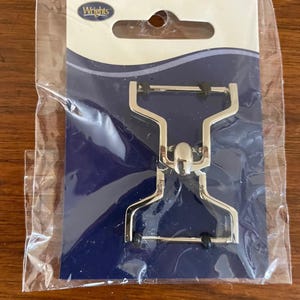 May include: A silver-colored metal clip, packaged in clear plastic, with the brand name "Wrights" visible. The clip has a unique shape with a central pivot and black rubber grips. The packaging has a blue and white design.