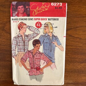 Könnte beinhalten: Ein Butterick-Schnittmusterumschlag mit der Nummer 6273, der Marie Osmond zeigt. Das Cover enthält Illustrationen von drei Hemdstilen: ein langärmeliges kariertes Hemd, ein kurzärmeliges blaues Hemd und ein kurzärmeliges geblümtes Hemd mit Gürtel.