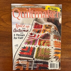 May include: A copy of Quiltmaker magazine with a colorful quilt on the cover. The magazine cover features the text "Spice up your Autumn with 5 Throws for Fall!" and "40 Years!" The magazine is on a wooden surface.