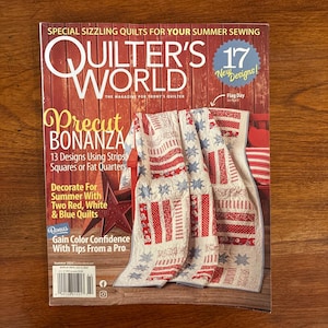 May include: A copy of Quilter's World magazine featuring a red, white, and blue quilt on the cover. The magazine's title is in large white letters, with the text "Precut Bonanza" and "17 New Designs!" also visible. The magazine is on a wooden surface.