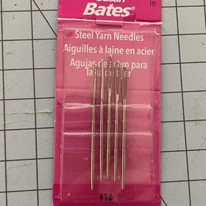 May include: A package of Susan Bates steel yarn needles. The pink package has the brand name and product information printed on it. The package contains five silver needles, each approximately 2 inches long. The needles are labeled as size #16.