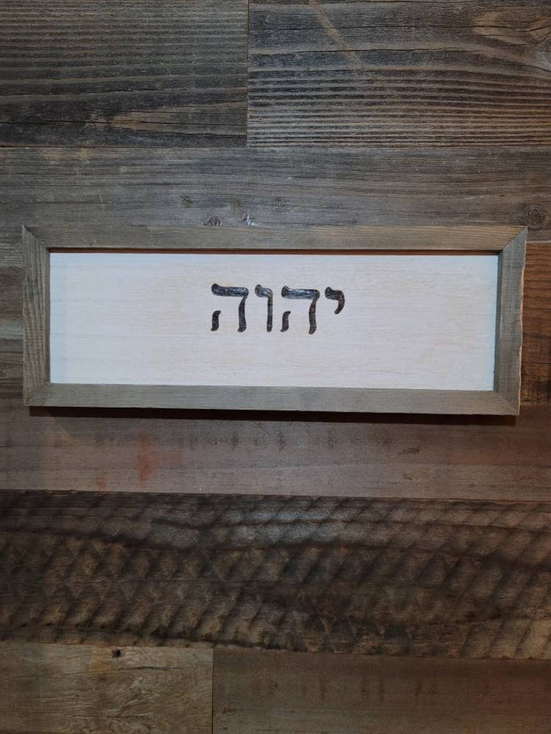 May include: A wooden sign with a light brown frame and a white background. The sign has the Hebrew word "קדושה" written in black.