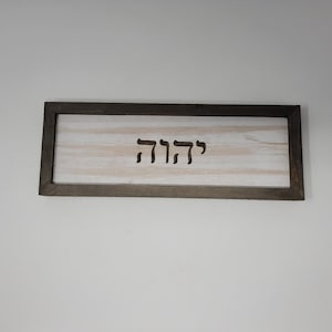 May include: A wooden sign with a dark brown frame and a white background. The sign has the Hebrew word "שלום" carved into it.