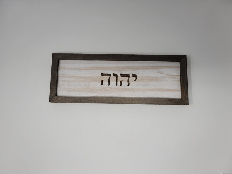 May include: A wooden sign with a dark brown frame and a white background. The sign has the Hebrew word "שלום" carved into it.
