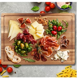 May include: A wooden serving board with a variety of food items, including cheese, salami, prosciutto, olives, figs, and dried tomatoes. The board is made of light brown wood and has a natural finish.