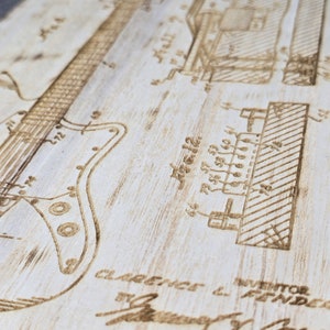 May include: A close-up of a wood-burned patent drawing of an electric guitar. The drawing includes the text "INVENTOR CLARENCE L. FENDER" and "ATTORNEY".